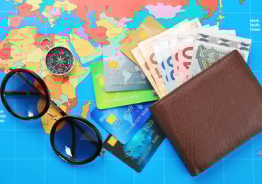Wallet with euro bills, credit cards, compass, and sunglasses on a colorful world map for travel budget planning.