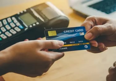 Customer handing a blue credit card to a merchant for payment at a retail POS terminal.
