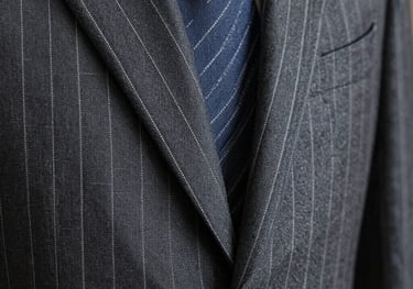 Close-up of pinstripe fabric on a bespoke suit, showing the hand-stitched lapel detail, luxurious texture, dark grey and white threads, European / Spanish.