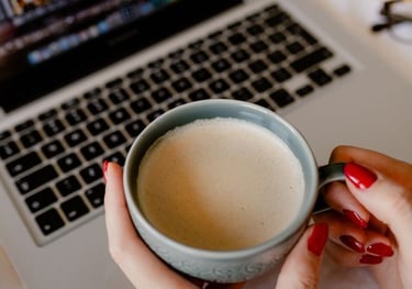 woman holding a cup of coffee in front of a laptop computer