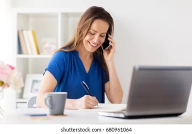 woman writing notes while talking on the phone and consulting her desktop computer