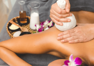 a woman getting a back massage with a thai herbal compress.