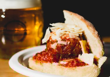 Meatball with marinara on a dinner roll with parmesan cheese shredded on top.