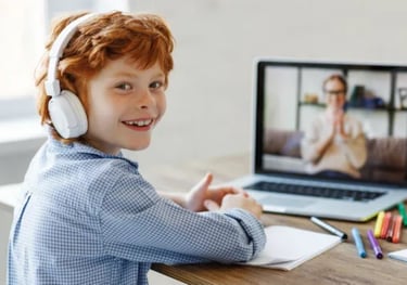 a young boy with headphones and a laptop, on the screen you can see his language tutor, both smiling