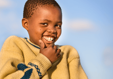 a young boy smiling and holding his hand up to his chin