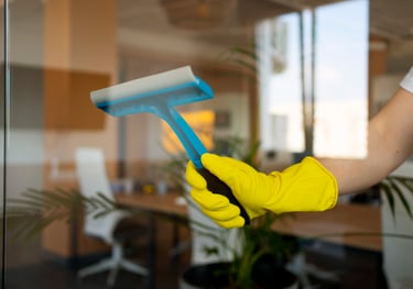 Close-up of blue-gloved hand using a squeegee for indoor window cleaning
