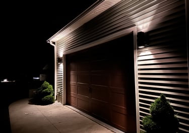 Modern outdoor garage wall sconces illuminating a brown garage door and vinyl siding at night.