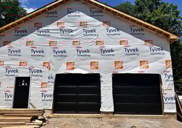 A new garage under construction featuring Tyvek HomeWrap vapor barrier and black garage doors.