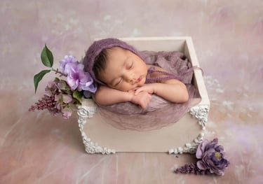 a newborn girl sleeping in a box with purple flowers