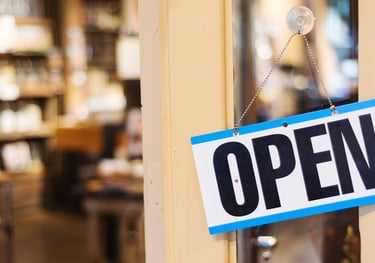 Open sign hanging on a glass door that is slightly open, with a store interior in the background.