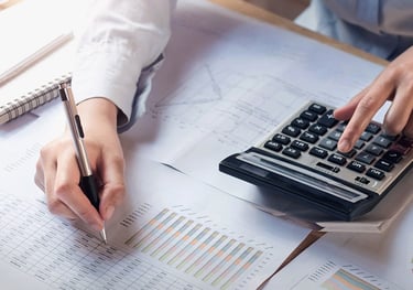 Partial view of an individual calculating and writing on a financial report or chart.