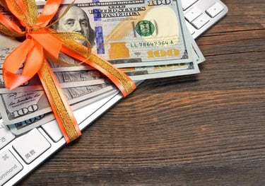 Partial view of hundred dollar bills resting on a computer keyboard.