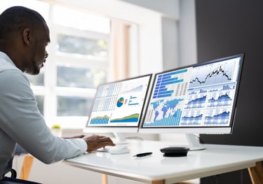 a man sitting at a desk with two monitors and a laptop