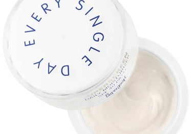 Open jar of eye cream with white lid labeled Supergoop