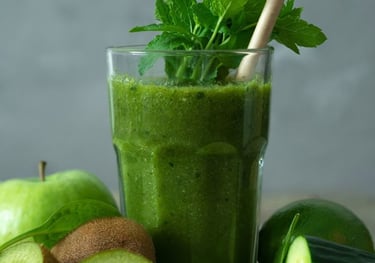 Copo de suco verde com folhas de hortelã, rodeado de ingredientes naturais como kiwi, pepino, maçã