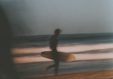 Blurred image of a person holding a surfboard, standing on the beach.