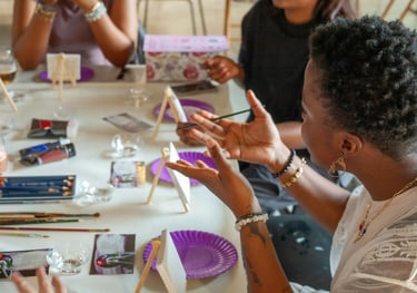 Group of people painting at a table with easels, brushes, and supplies — a creative, social activity