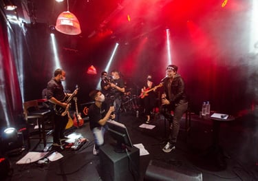 banda tocando num palco com fundo preto e luzes vermelhas e brancas