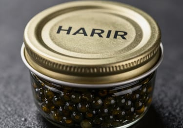 A macro photograph of a premium HARIR caviar vial with a metallic gold cap. The glass reflects a sophisticated dark environment. Professional product photography.
