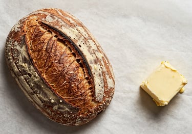 A flat lay of artisanal sourdough bread and fresh butter on a crisp parchment background, styled for a North American / US bakery brand.