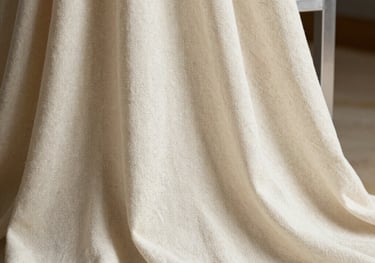 A close-up shot of ivory linen fabric with a subtle herringbone weave, draped over a silver display stand, International / Western elegance.