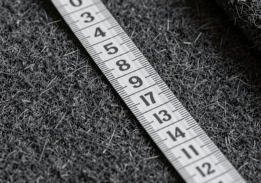 A macro shot of luxurious charcoal cashmere fabric being measured with a silver tape measure, illustrating precision and luxury, International / Western.