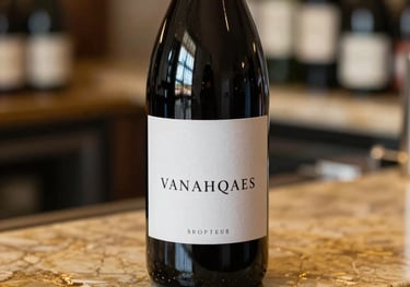 A detailed close-up shot of a bottle of red wine standing on a gold-veined marble counter. The label is minimalist and elegant. Soft North American boutique shop lighting creates a sophisticated rim light on the bottle glass.