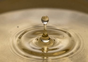 A macro shot of a single drop of mezcal creating golden ripples in a pool of liquid. Soft focused antique gold lighting.