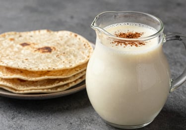 A frosted pitcher of creamy Horchata with a sprinkle of cinnamon on top, placed next to handmade tortillas in a North American / Mexican setting.