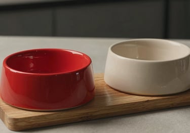A pair of ergonomic ceramic cat bowls, one intense crimson red and one beige, on a minimalist wooden stand. Professional product photography.