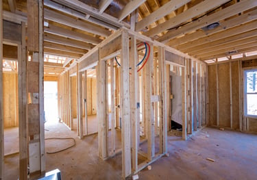 Interior view of a home under construction showing wood stud framing, exposed plumbing, and electrical rough-in