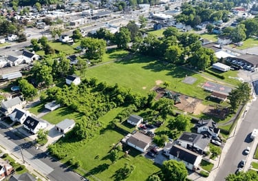 Aerial drone view of a vacant infill lot surrounded by a residential neighborhood and nearby park.