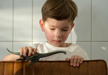 a young boy sitting in a suitcase with a dinosaur toy