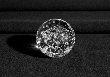 A clear glass sphere with bubbles inside, resting on a textured black surface. 