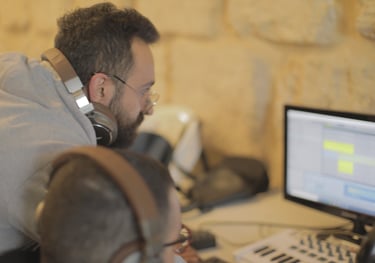 a man with headphones and a student on the computer learning music production