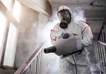 a man in a white suit and a gas mask disinfecting a stair railing