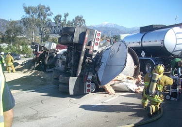 a firefighter standing next to a fallen chemical truck with a hose attached to it