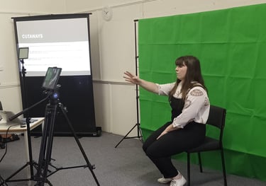Laura sits in front of a greenscreen and in front of an ipad teaching a class about cutaways