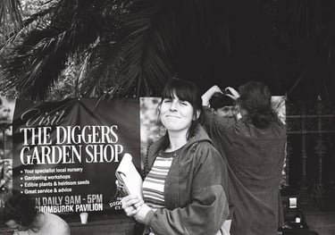 A black and white 35mm photo of Laura holding a clipboard. Smiling on set as actors fix their hair