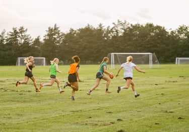 A group of women from the West London Wildcats run across a field kicking an AFL Football.