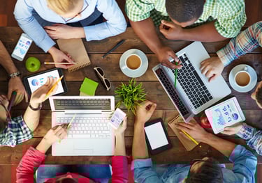 a group of people sitting around a table with laptops