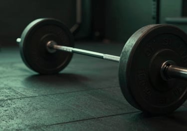 Close up of a barbell with rubber plates in a dark minimalist gym. Low angle shot, atmospheric lighting with subtle #4A8C67 green glow on the floor.