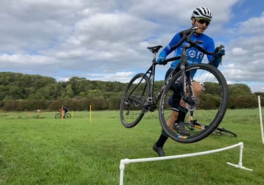 A cyclocross rider carrying their bike over hurdles