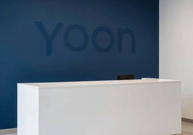 A minimalist photo of a sleek white reception area with a deep blue accent wall, featuring a subtle YOON logo, South Asian / Pakistani interior style, clean Apple-like aesthetics.