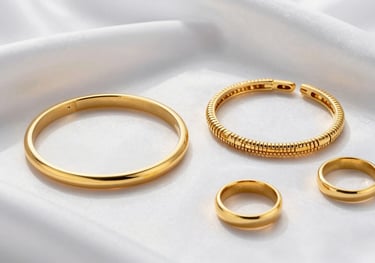 A professional flat-lay photograph of a collection of gold bracelets and rings resting on a piece of white silk, with soft shadows and high-end lighting, representing luxury jewelry design.