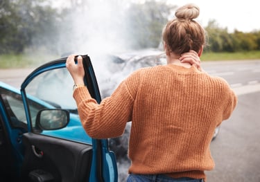 Woman holding neck after car accident with two cars facing each other and smoke coming from one car.