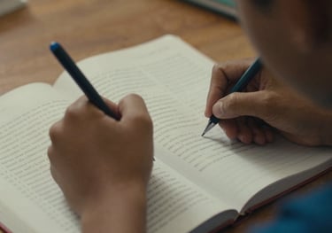A close-up of a student's hands taking notes in a language textbook. South American / Brazilian setting, warm lighting, educational focus.