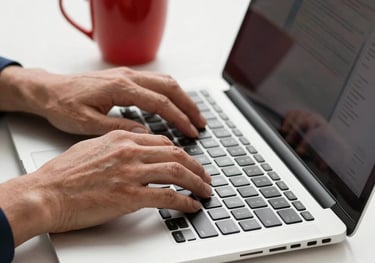 Close-up of a professional's hands typing on a high-end laptop next to a red coffee cup on a white desk. Minimalist and efficient style.