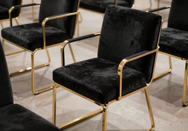 Photography of charcoal black velvet chairs with sleek metallic gold frames arranged in a geometric pattern on a polished floor. North American / US luxury rental gallery style.