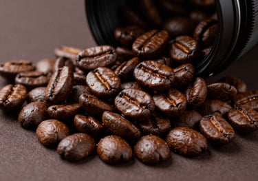 A studio product shot of freshly roasted, oily dark coffee beans cascading onto a dark brown surface. Sharp focus, professional lighting, reflecting premium quality.